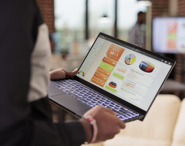 Employee holding laptop with business diagrams in company office, management presentation of diagrams and graphs on computer screen. Data report and research information on pc. Close up.