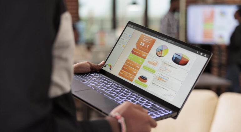 Employee holding laptop with business diagrams in company office, management presentation of diagrams and graphs on computer screen. Data report and research information on pc. Close up.