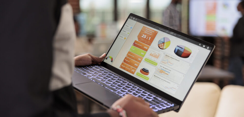 Employee holding laptop with business diagrams in company office, management presentation of diagrams and graphs on computer screen. Data report and research information on pc. Close up.